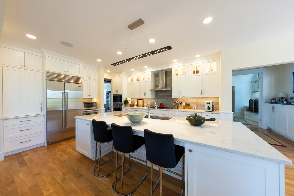 A white kitchen with a long island and black bar stools