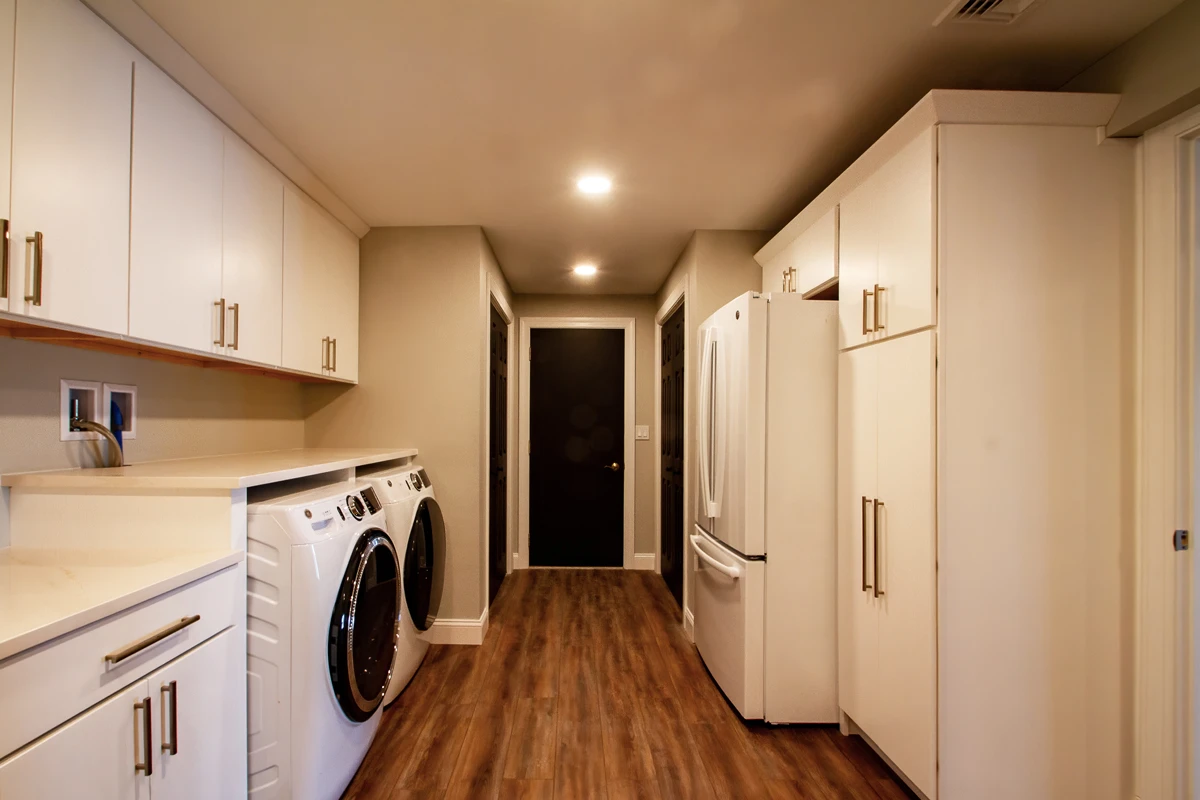 A finished laundry room with a front-loading washer and dryer, white cabinets and vinyl plank floors