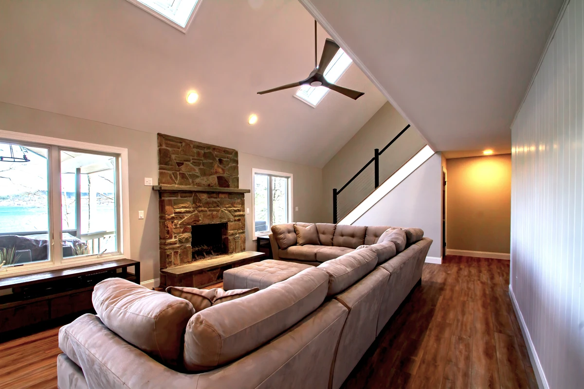 A vaulted living room with a stone fireplace, a sectional sofa and new plank flooring
