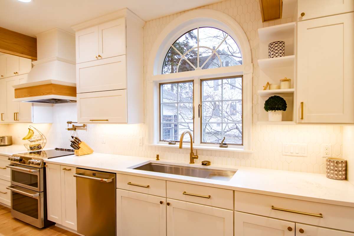 A kitchen sink and brass faucet under an arched window