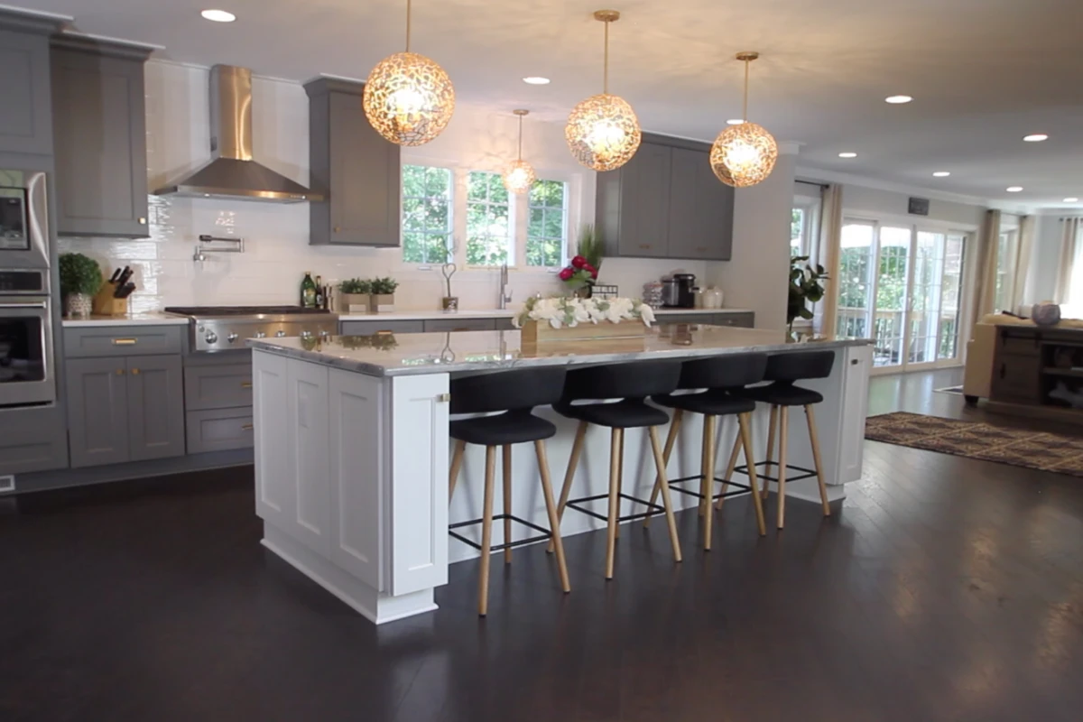 An open kitchen with a white island, pendant lights and bar stools, the living room beyond it