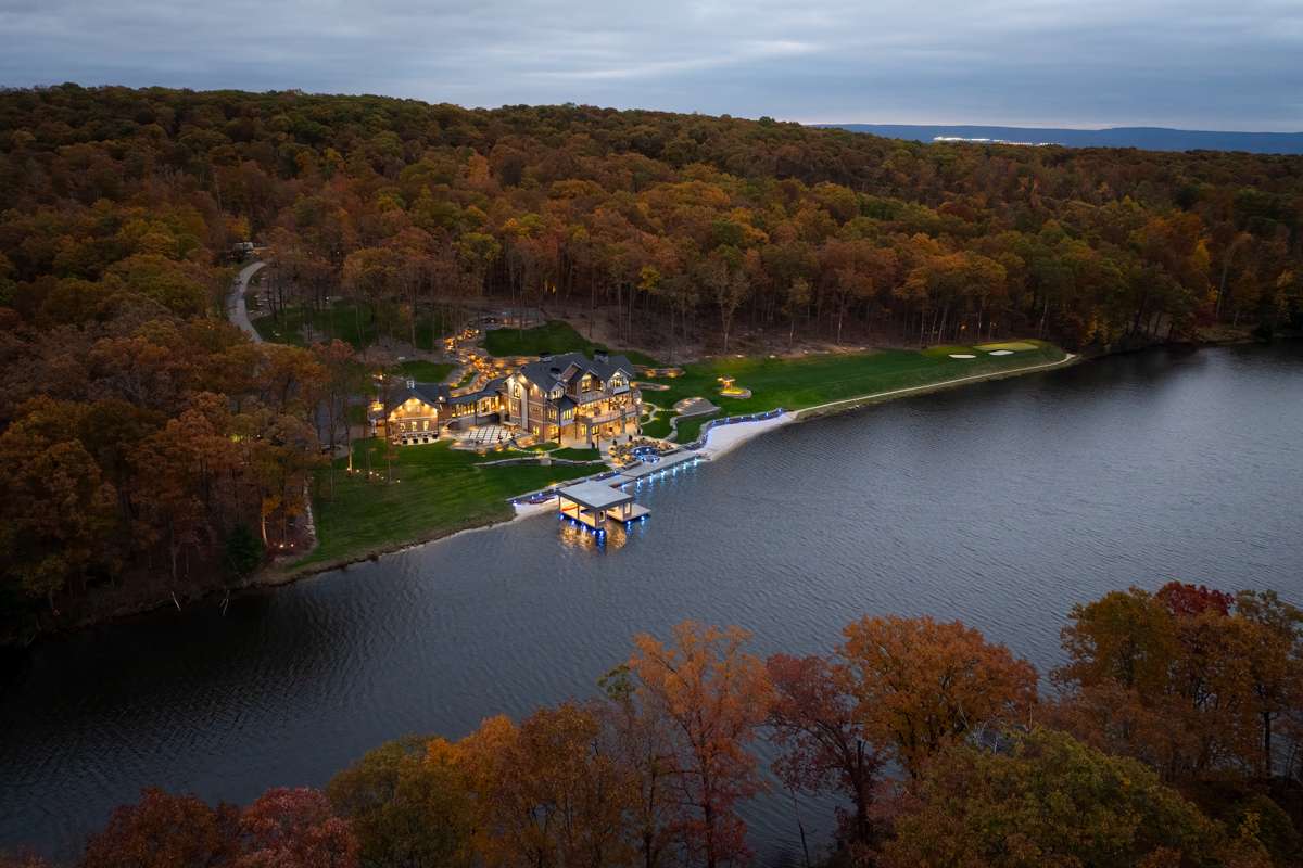 An aerial view of a lakefront estate at the water's edge, wooded hills around the lake