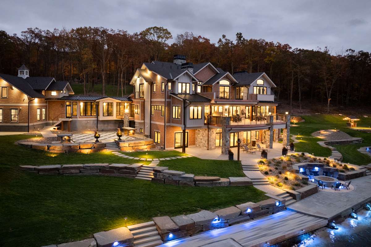 A new lakefront home lit up at dusk, its paths and terraces glowing