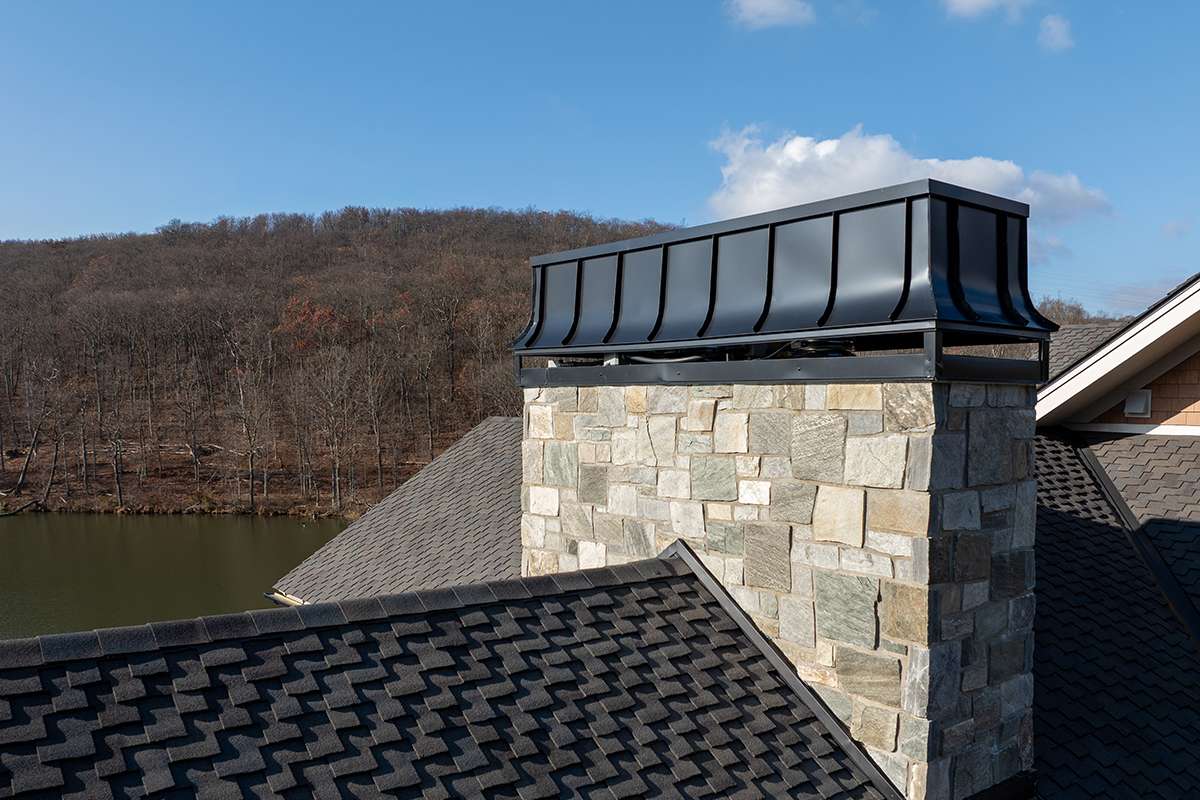 A stone chimney with a metal cap on a new shingle roof
