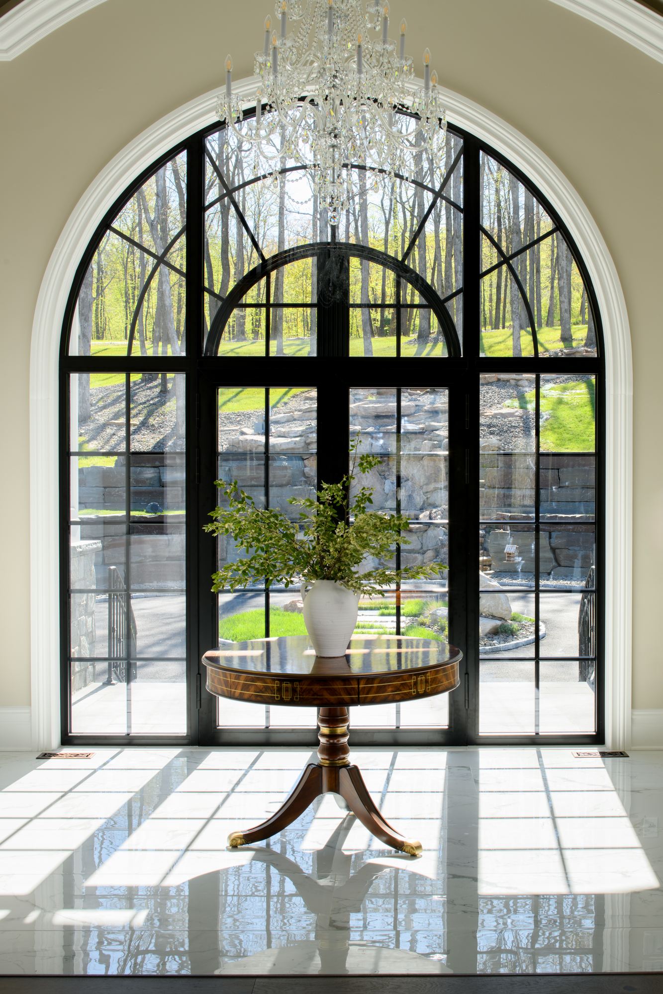 Arched black-framed doors and a round table on a marble floor in the foyer