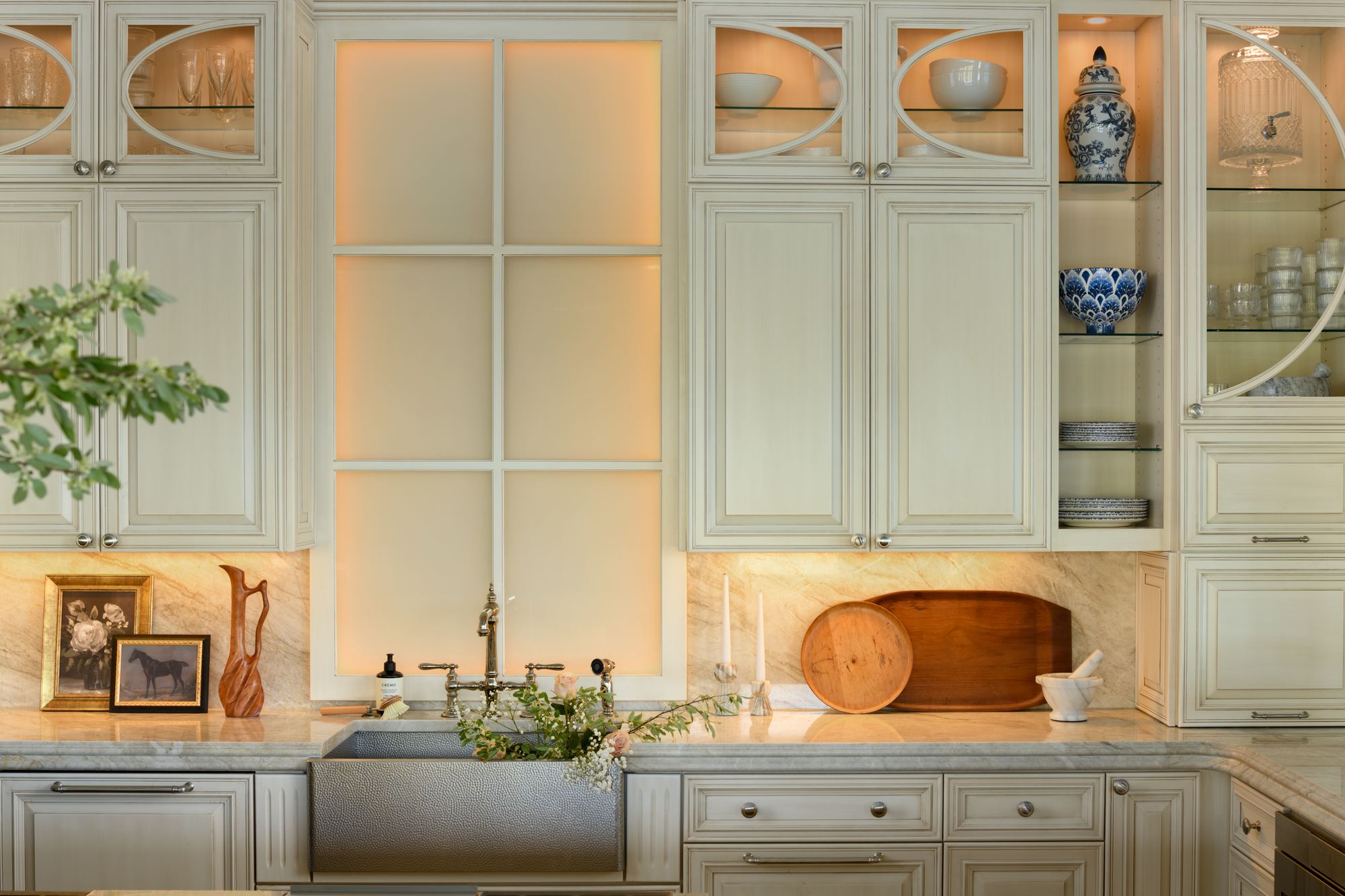 Kitchen with lit glass-front cabinets, a farmhouse sink and a marble backsplash