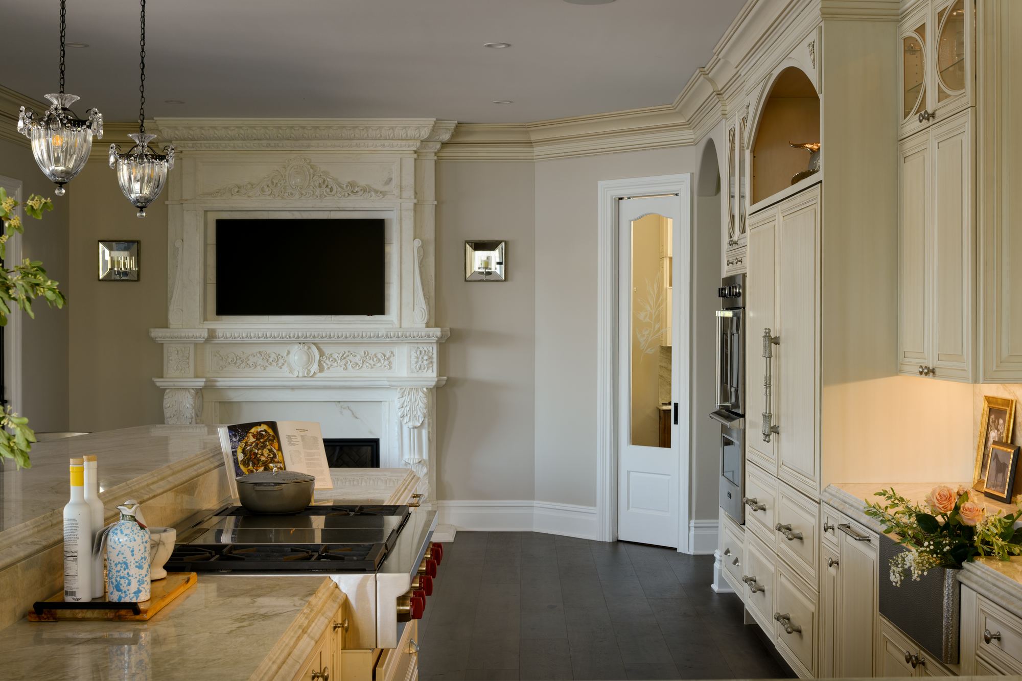Kitchen island under crystal pendants, a carved fireplace mantel at the far end