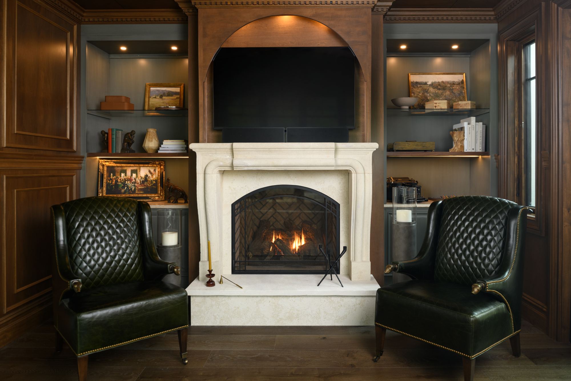 Wood-paneled den with a stone fireplace, built-in shelves and leather wing chairs