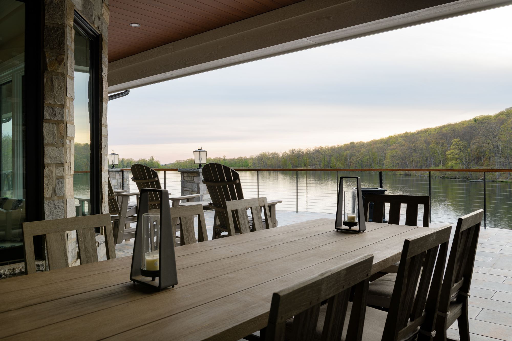 Long dining table on the covered patio, the lake beyond the cable railing