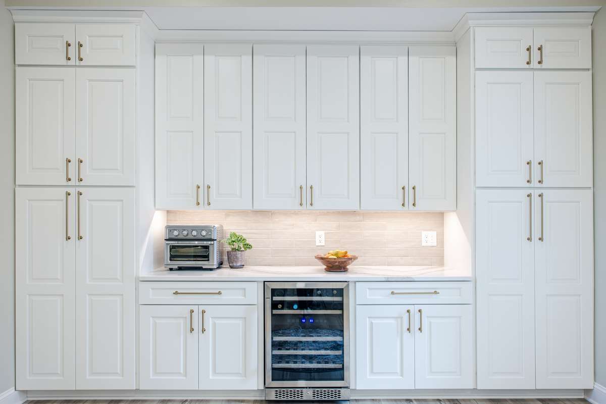 A full wall of custom white kitchen cabinets around a wine fridge