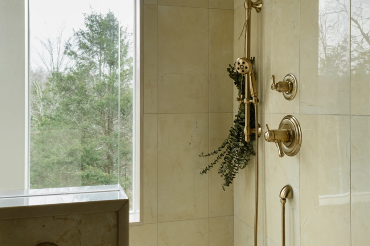 A tiled shower with a handheld shower head on a slide bar beside a window