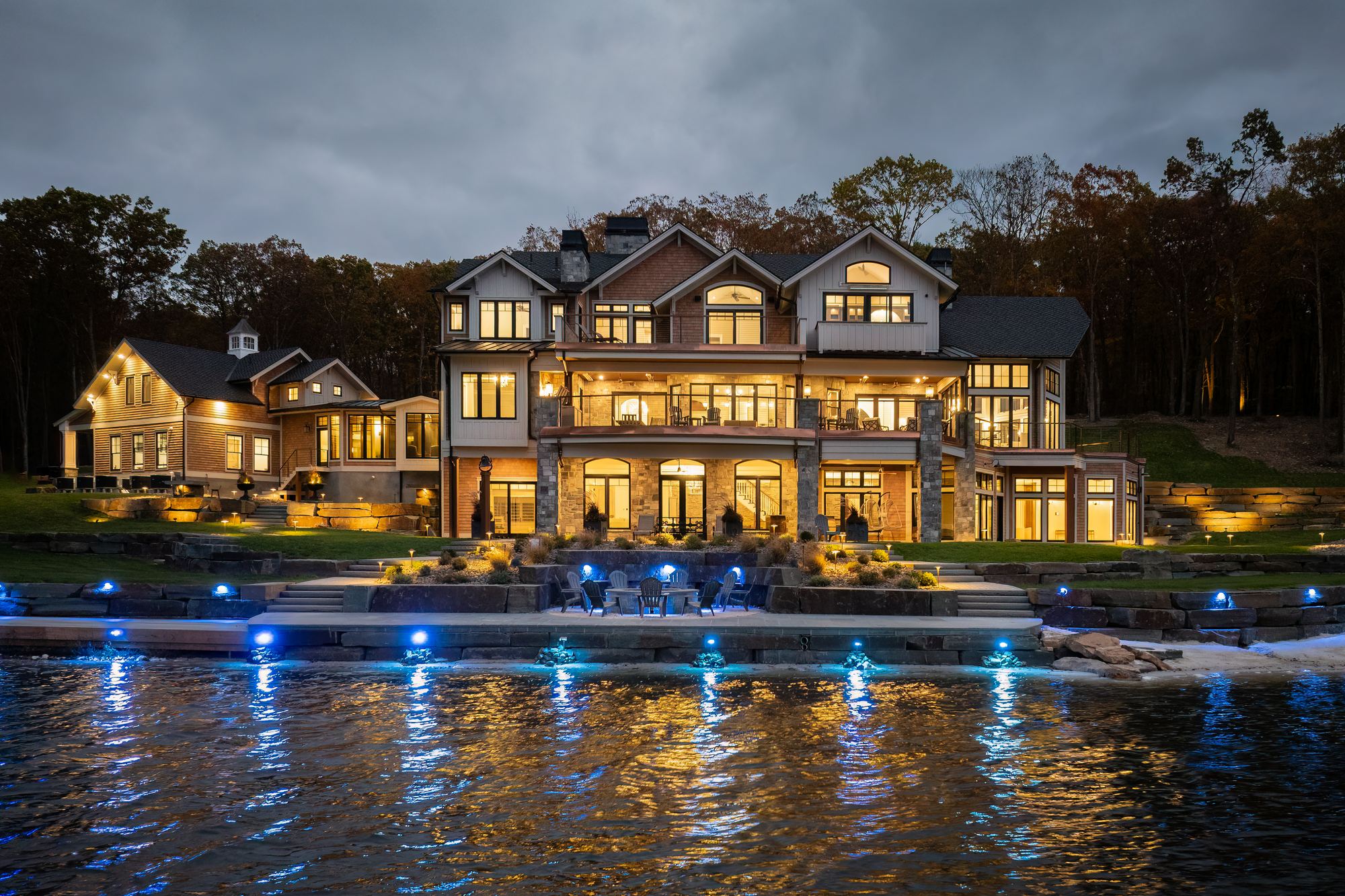The estate lit at dusk, seen from the water with dock lights glowing