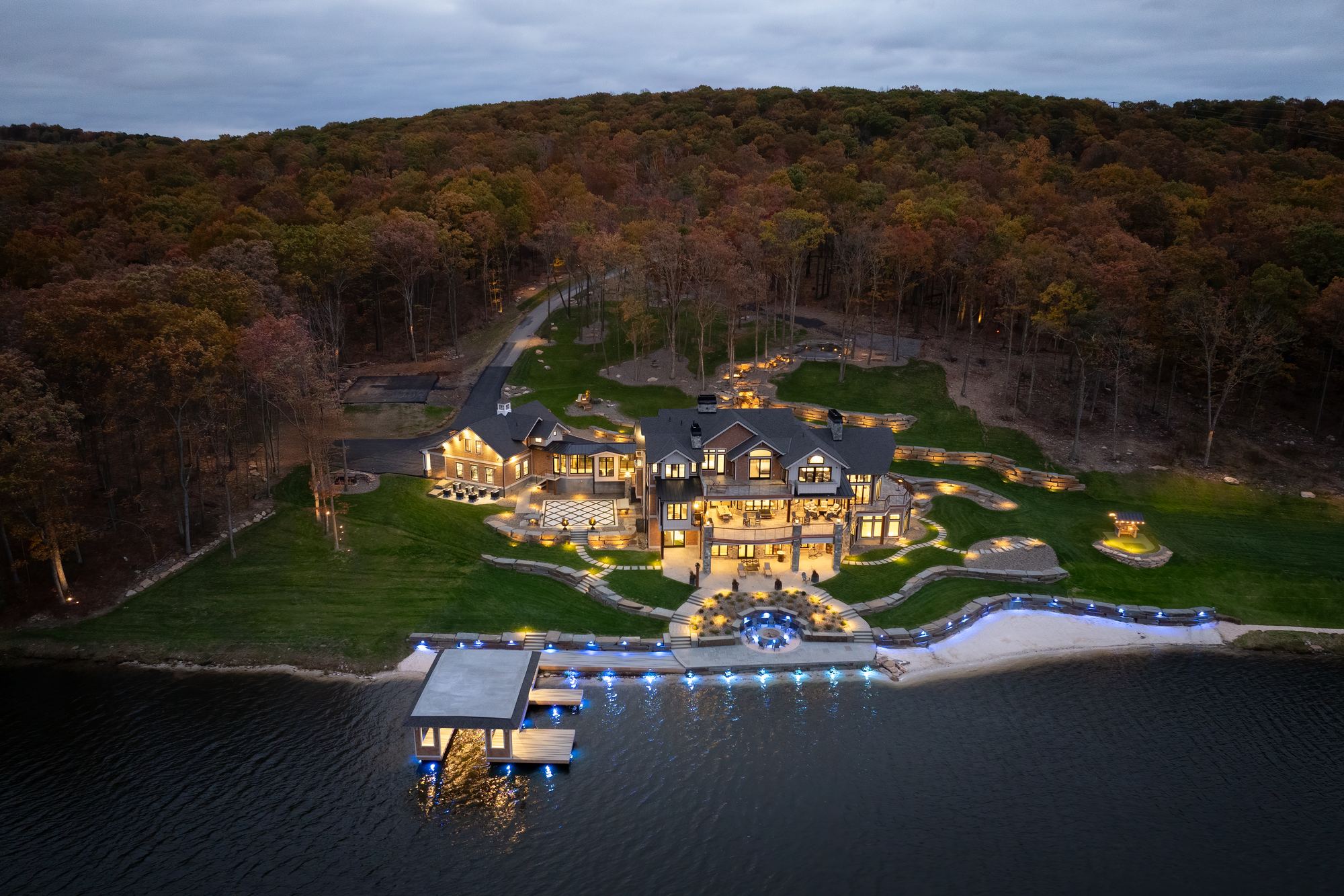 Aerial view of the estate at dusk, its lit landscape and boathouse on the shore