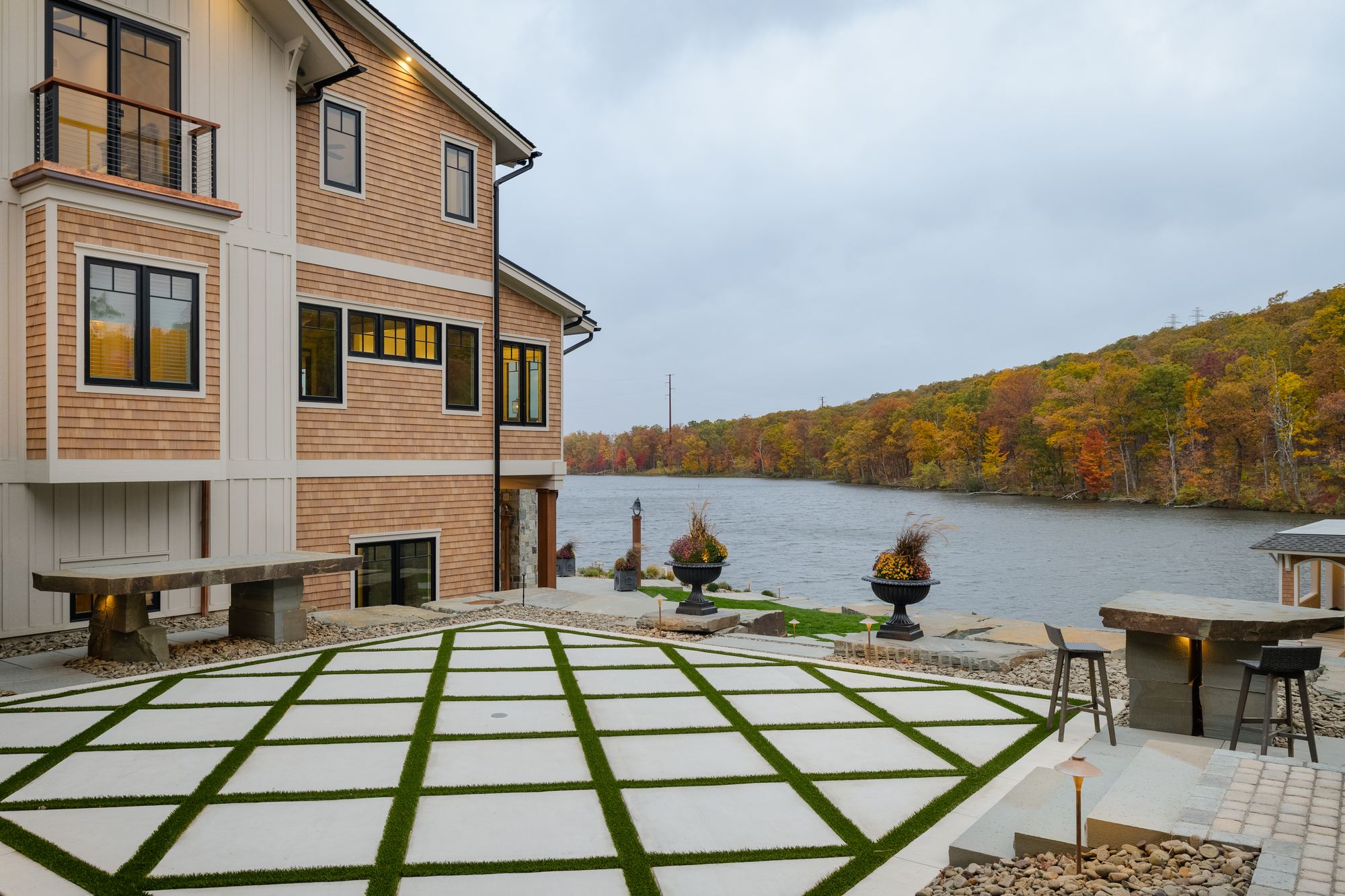 Stone terrace set in a grass grid, with an outdoor kitchen and the lake beyond