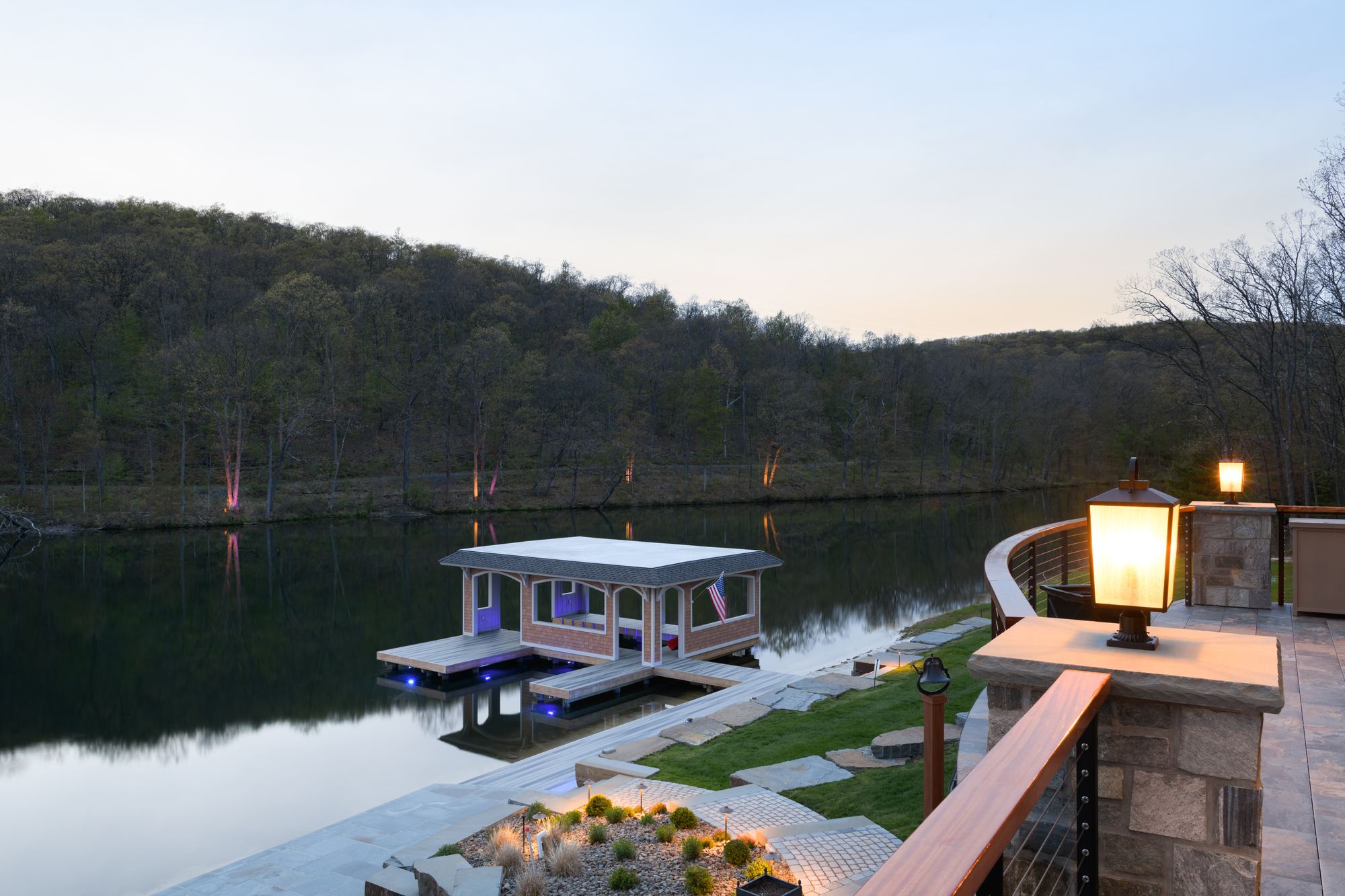 Lit boathouse on the lake at dusk, seen past a lantern pier