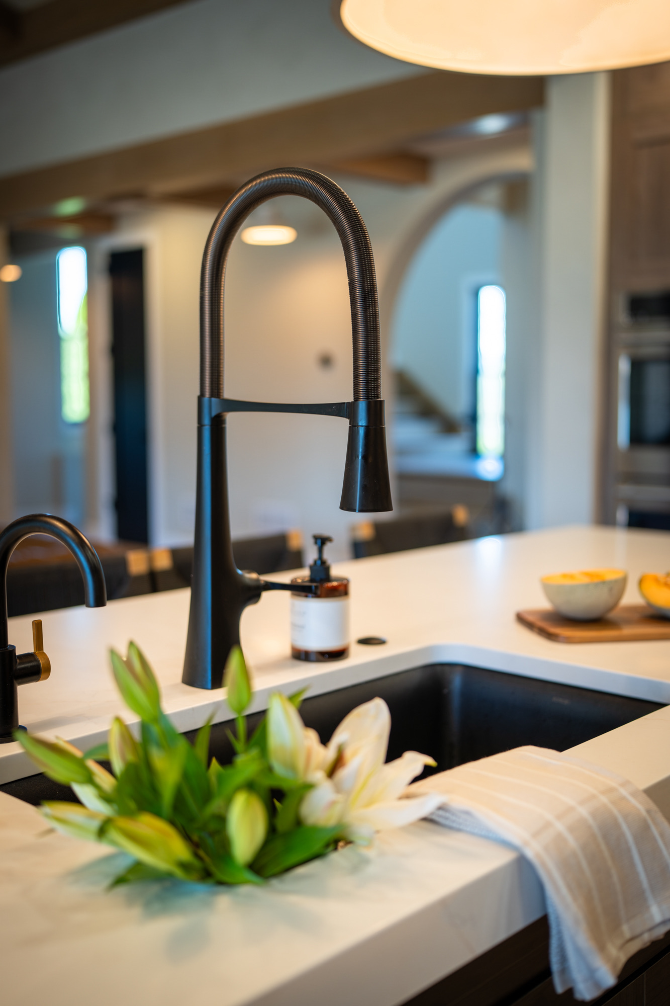 Black pull-down faucet over a quartz island, the arched hall beyond