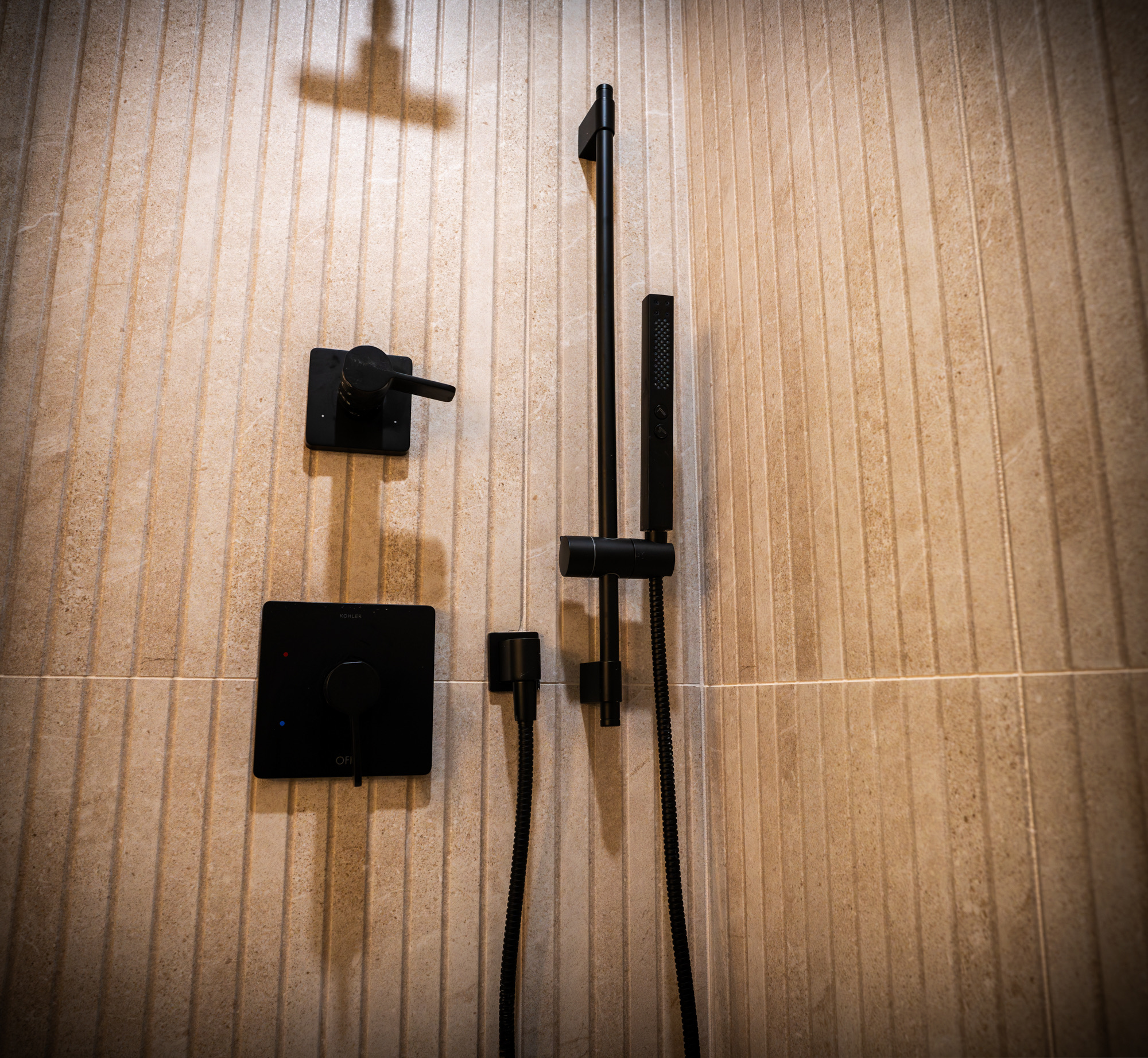 Matte black shower valve and hand shower on fluted stone tile