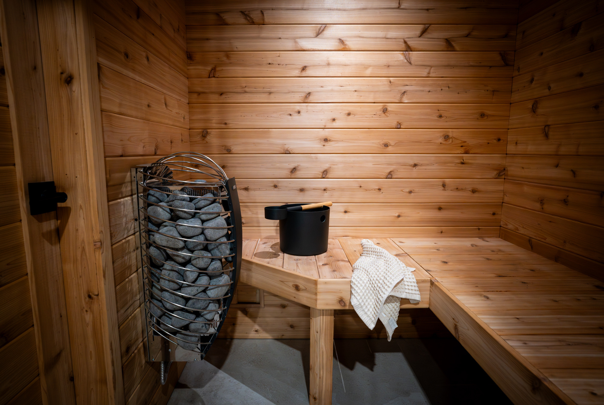 Cedar-lined home sauna with a stone heater and corner bench
