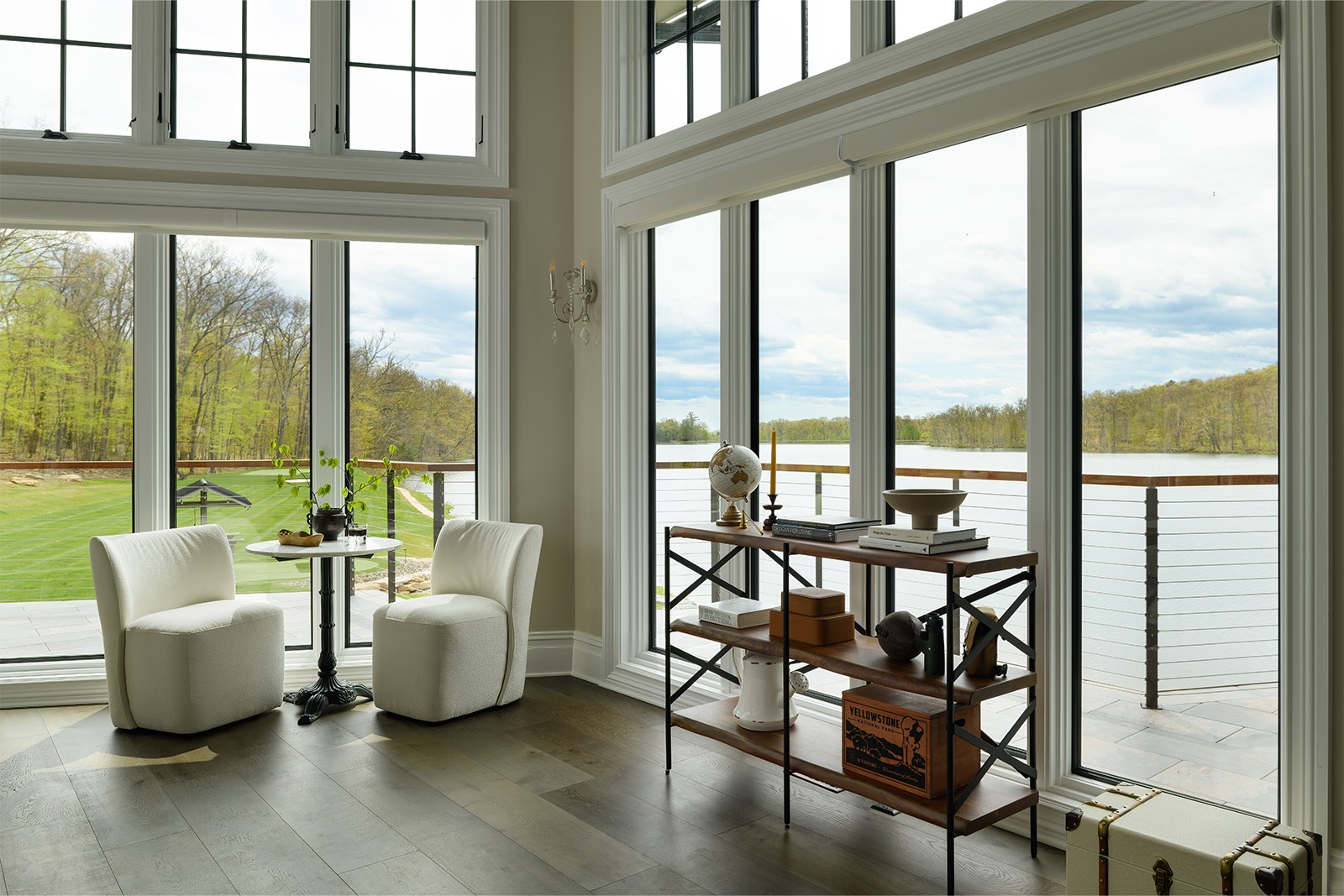 Two storeys of white-framed windows looking out on a lake, with two armchairs and a bistro table
