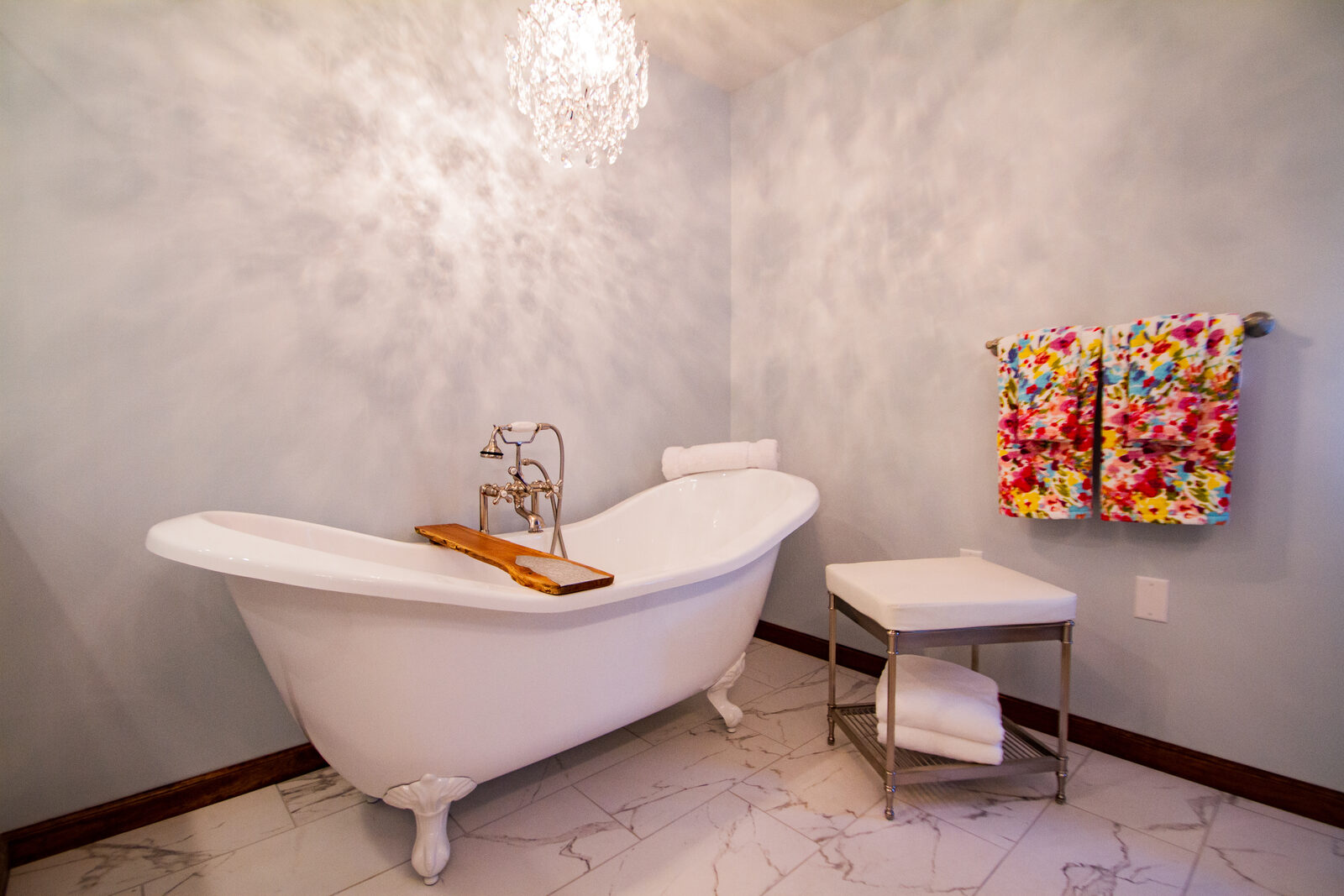 A clawfoot tub on a marble tile floor under a small crystal chandelier