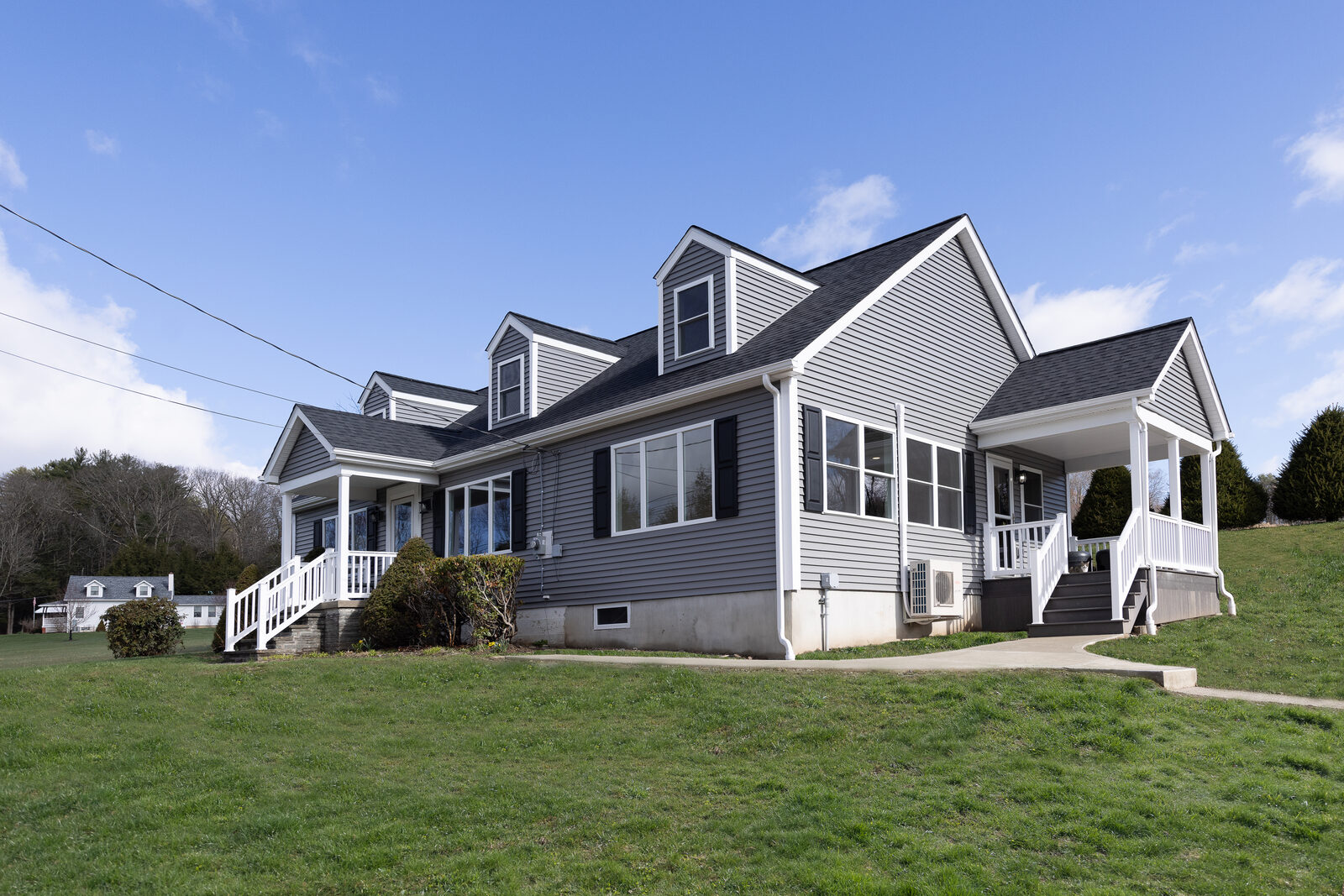 A grey Cape Cod house with a new roof, dormers and white porches on both ends