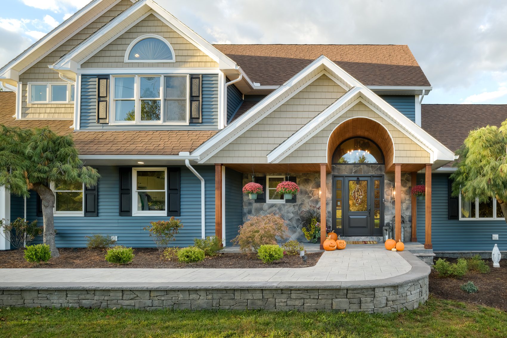 A two-storey home in new blue siding with shake gables and a stone-and-cedar arched entry