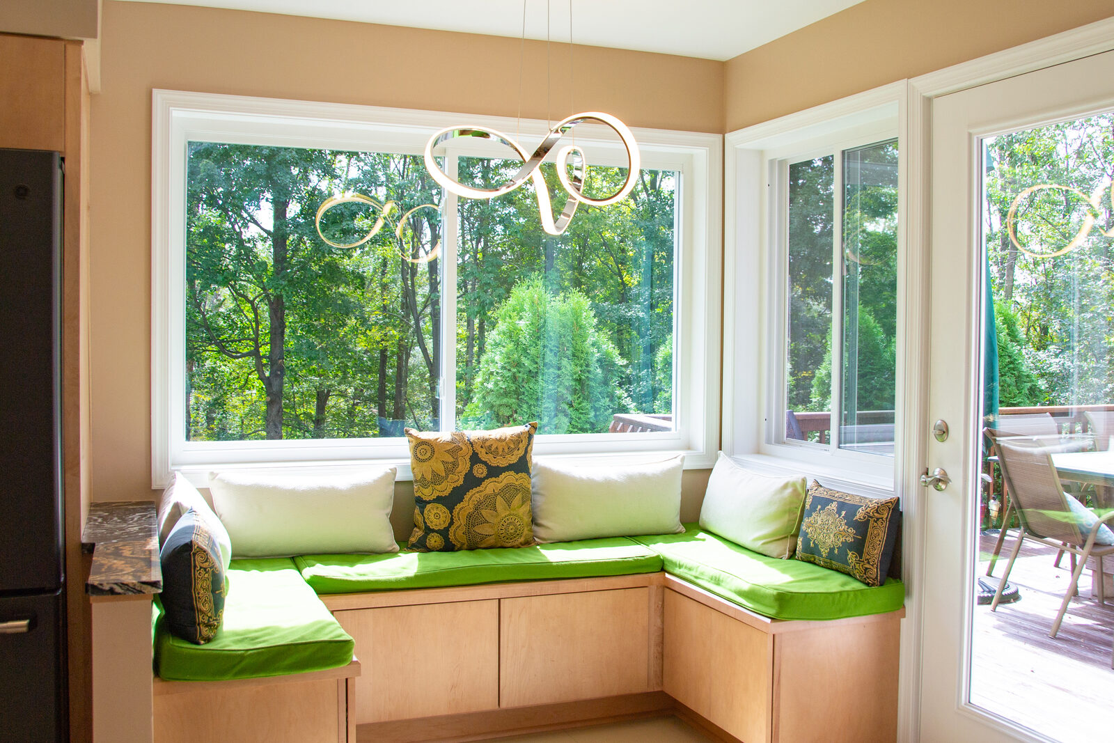 A built-in window seat with green cushions in a bright kitchen nook, trees outside on three sides