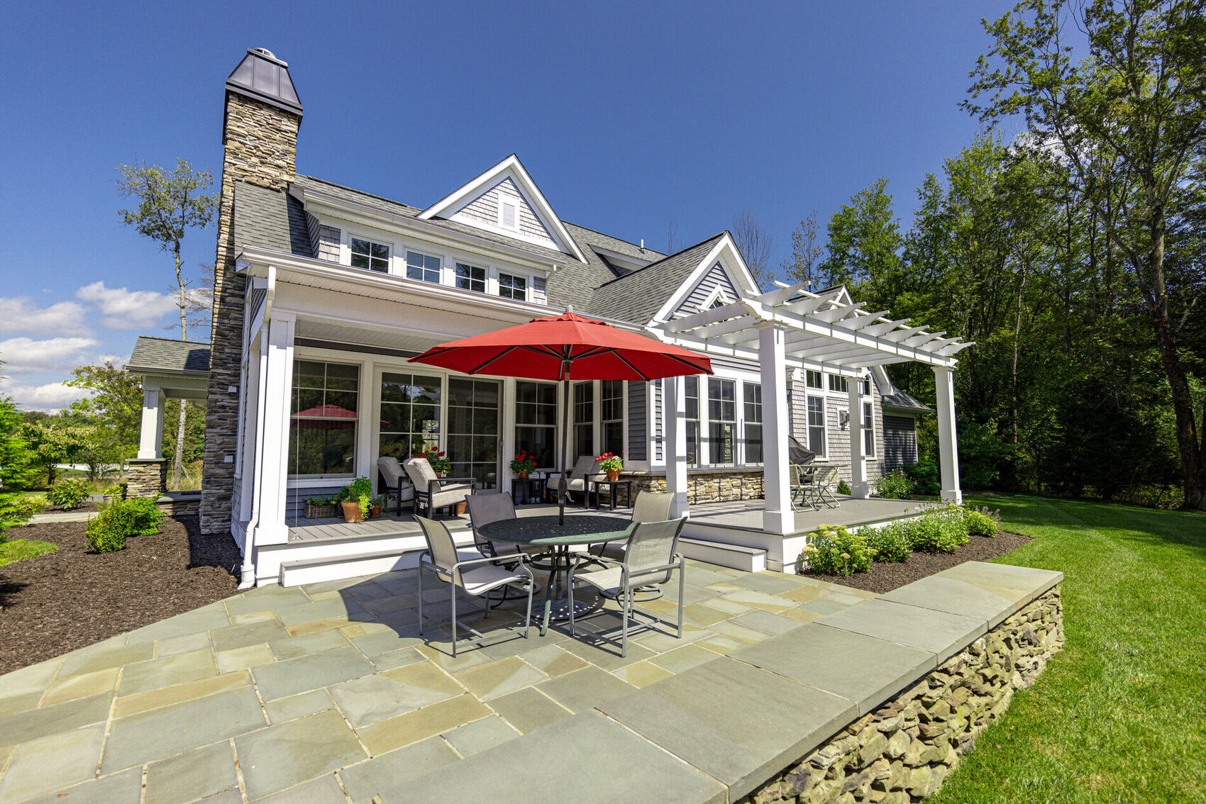 A bluestone patio outside a wall of patio doors and windows under a pergola
