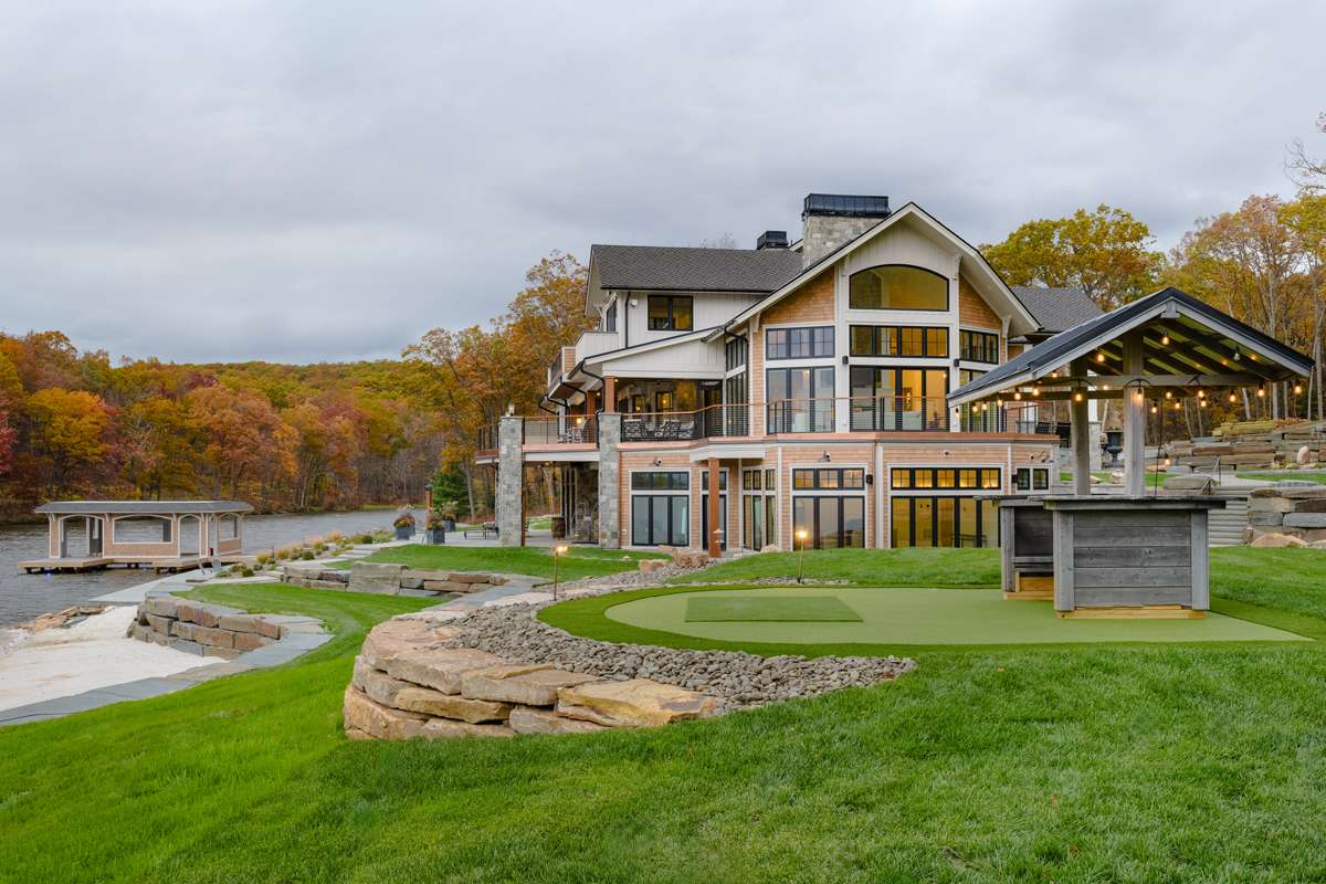 A green lawn, planted beds and a curved stone wall below a lakeside home