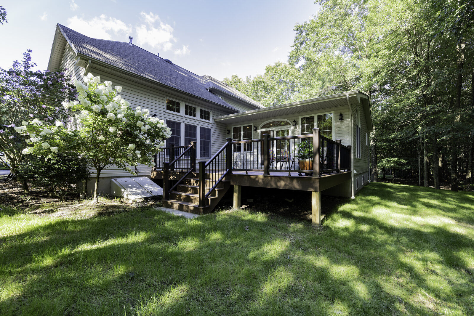 The back of a house with a new addition in matching siding, a wall of windows and a deck