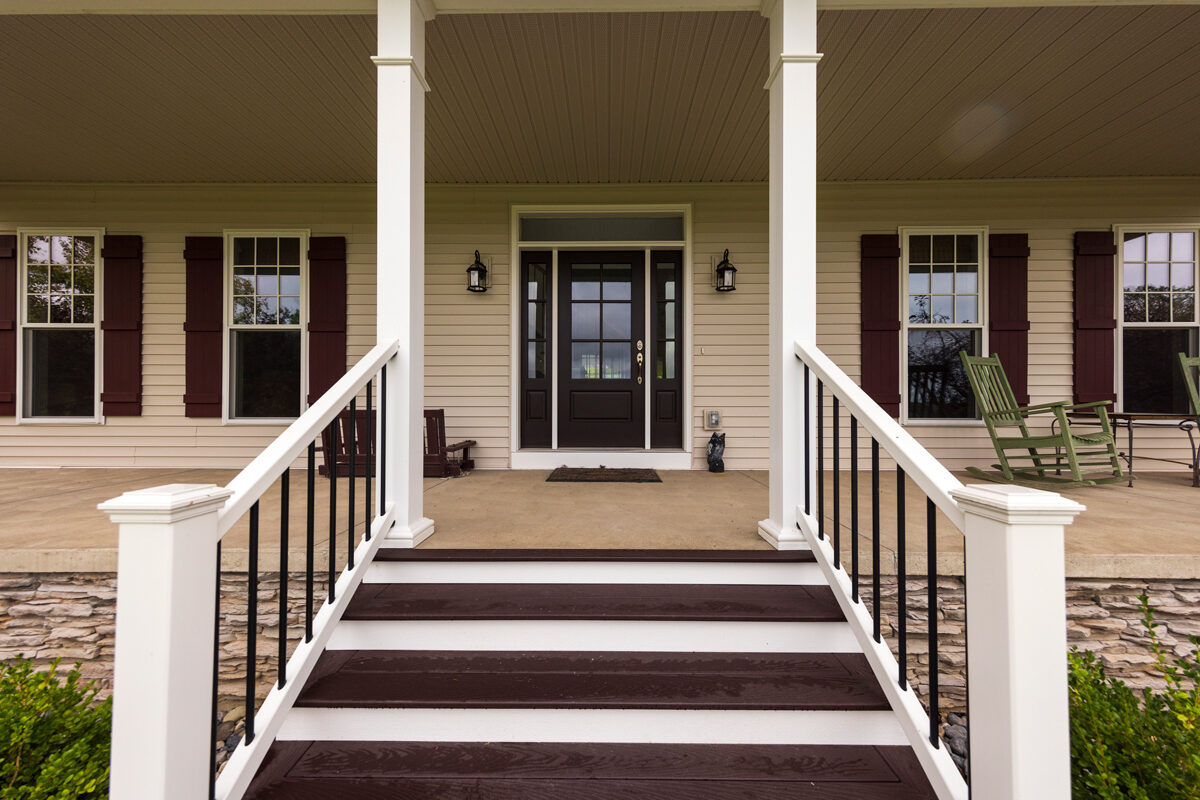 A new front entry door with sidelights, framed by white porch columns and steps with black railings
