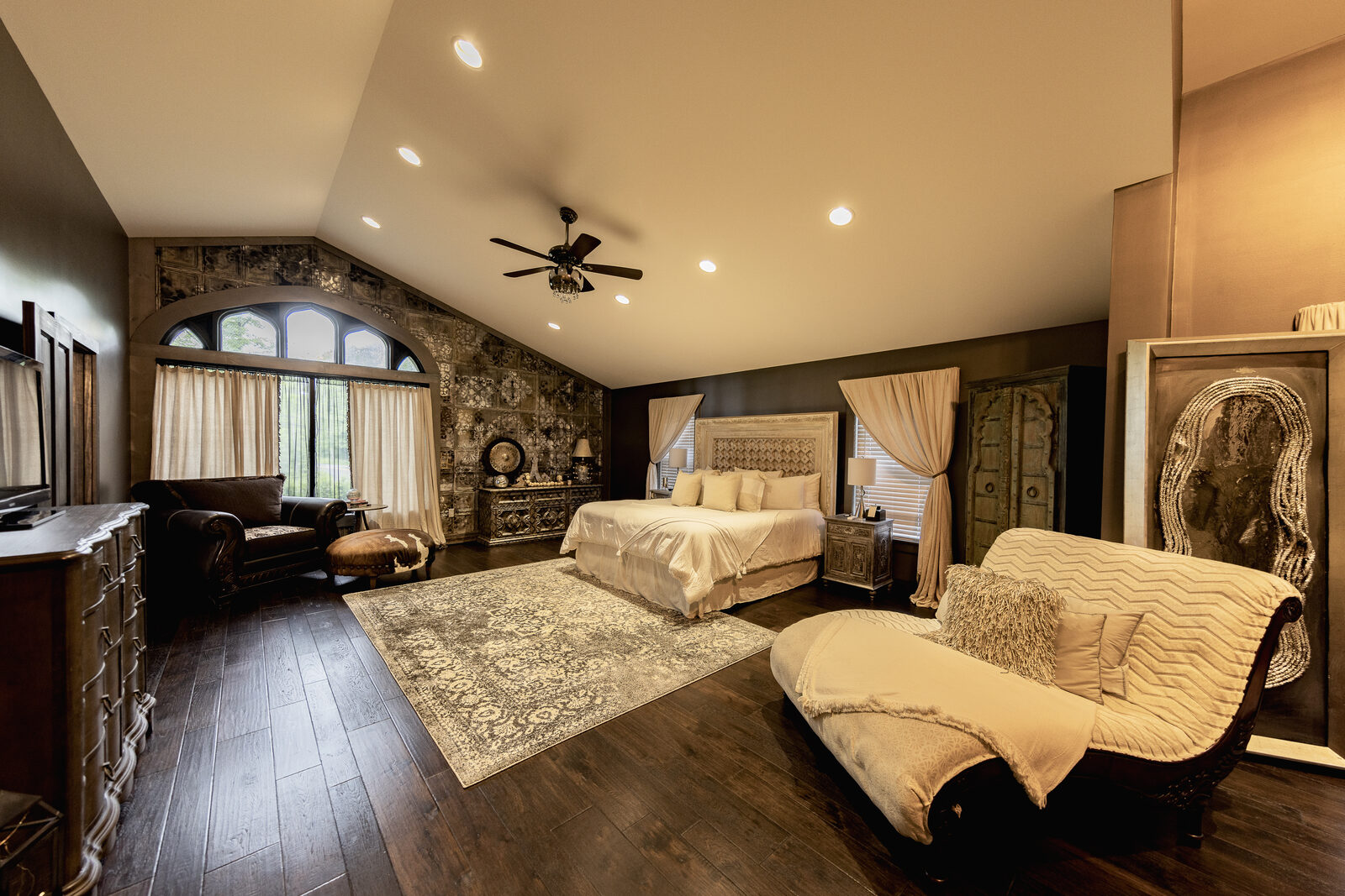 A primary bedroom suite with a vaulted ceiling, a dark wood floor and an arched window