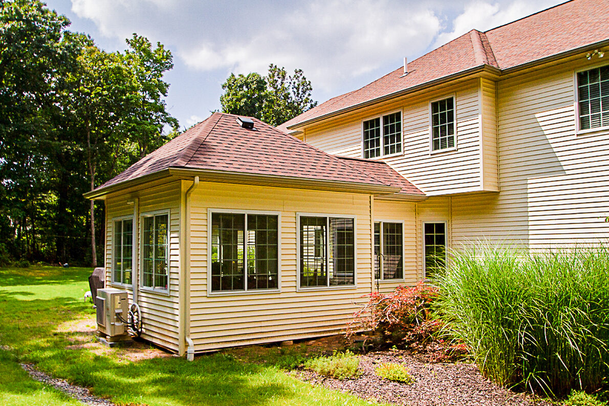 A cream house with a new addition whose roof meets the main roof above a row of windows