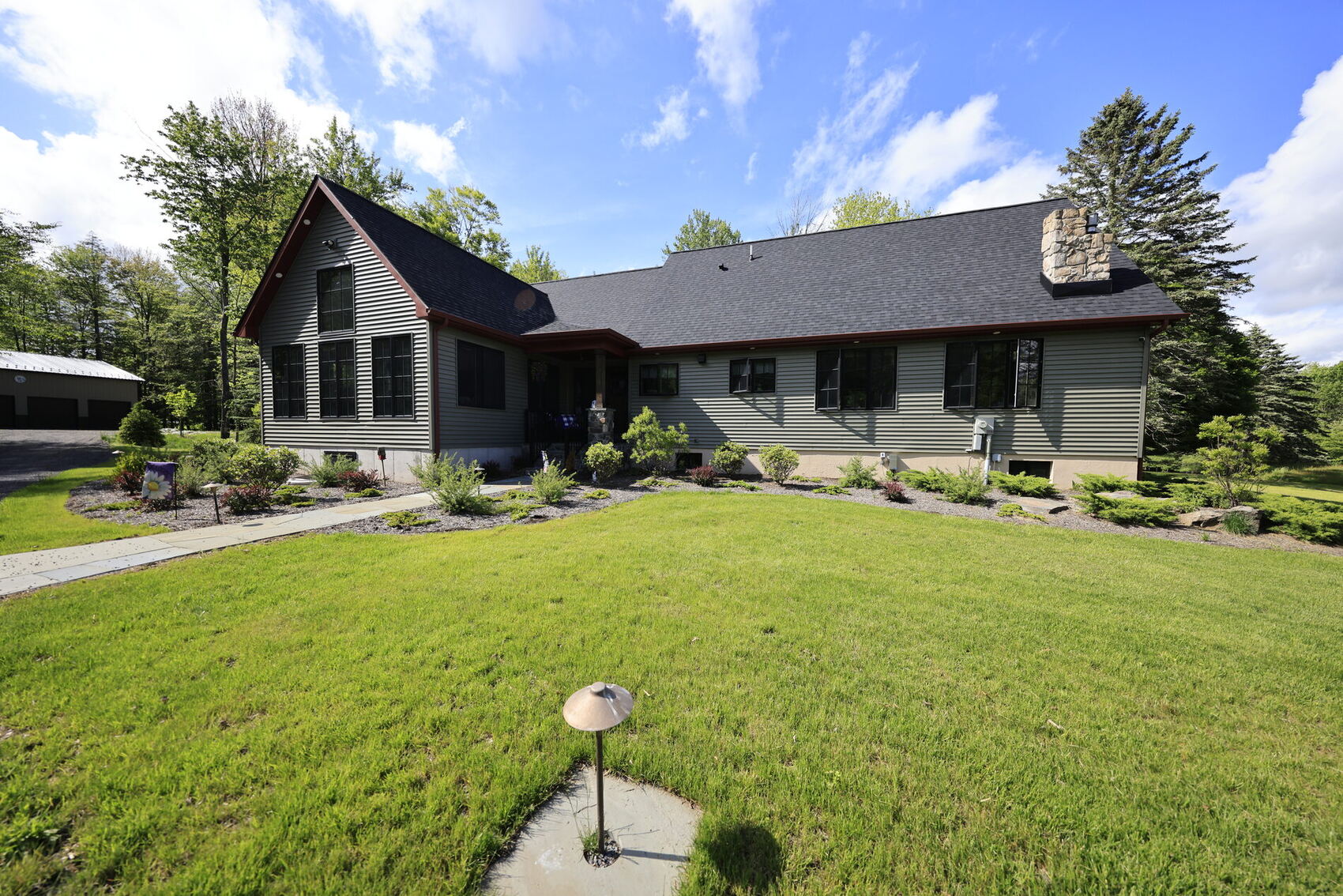 A single-story home with grey siding, a stone chimney and a bluestone walk