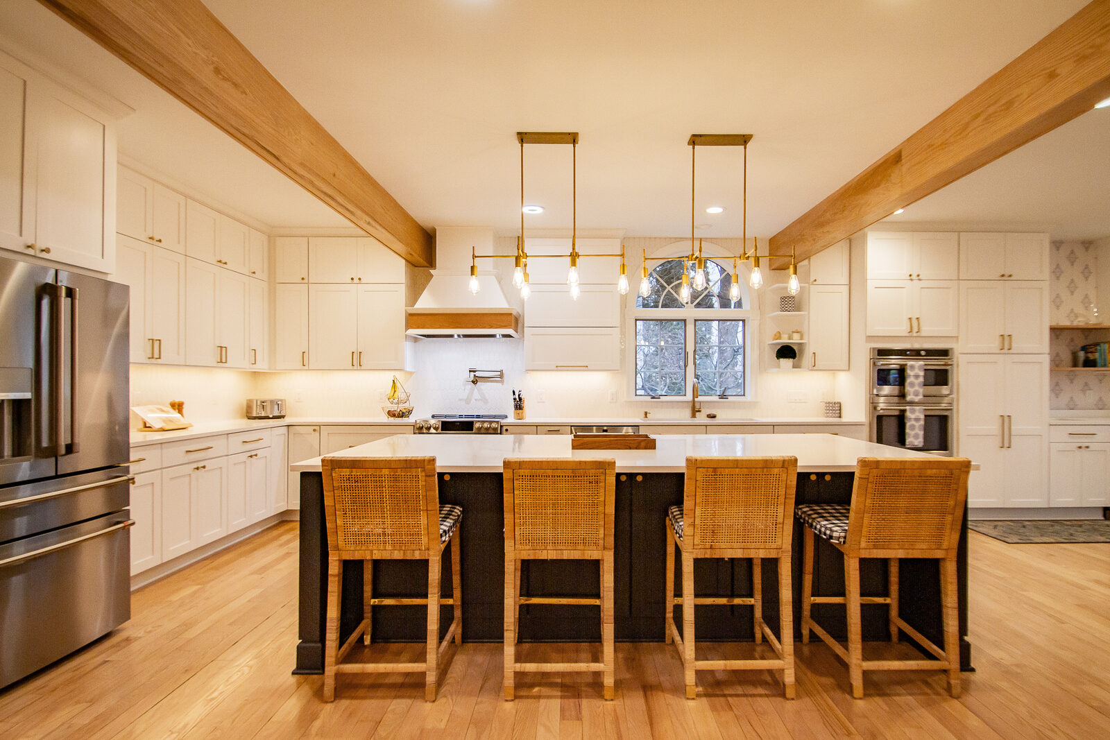 A remodeled kitchen with white cabinetry, exposed wood beams and a long island with seating for four