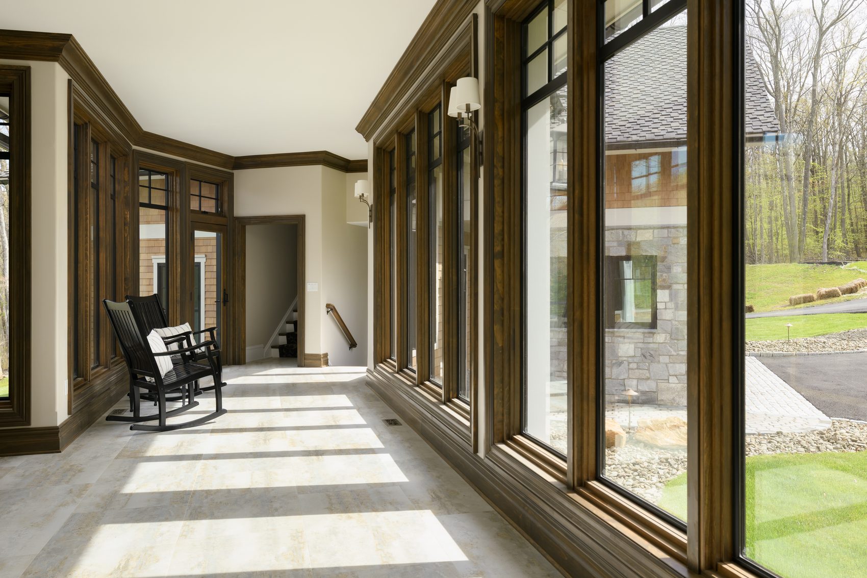 Sun through a wall of tall wood-trimmed windows across a tiled sunroom floor