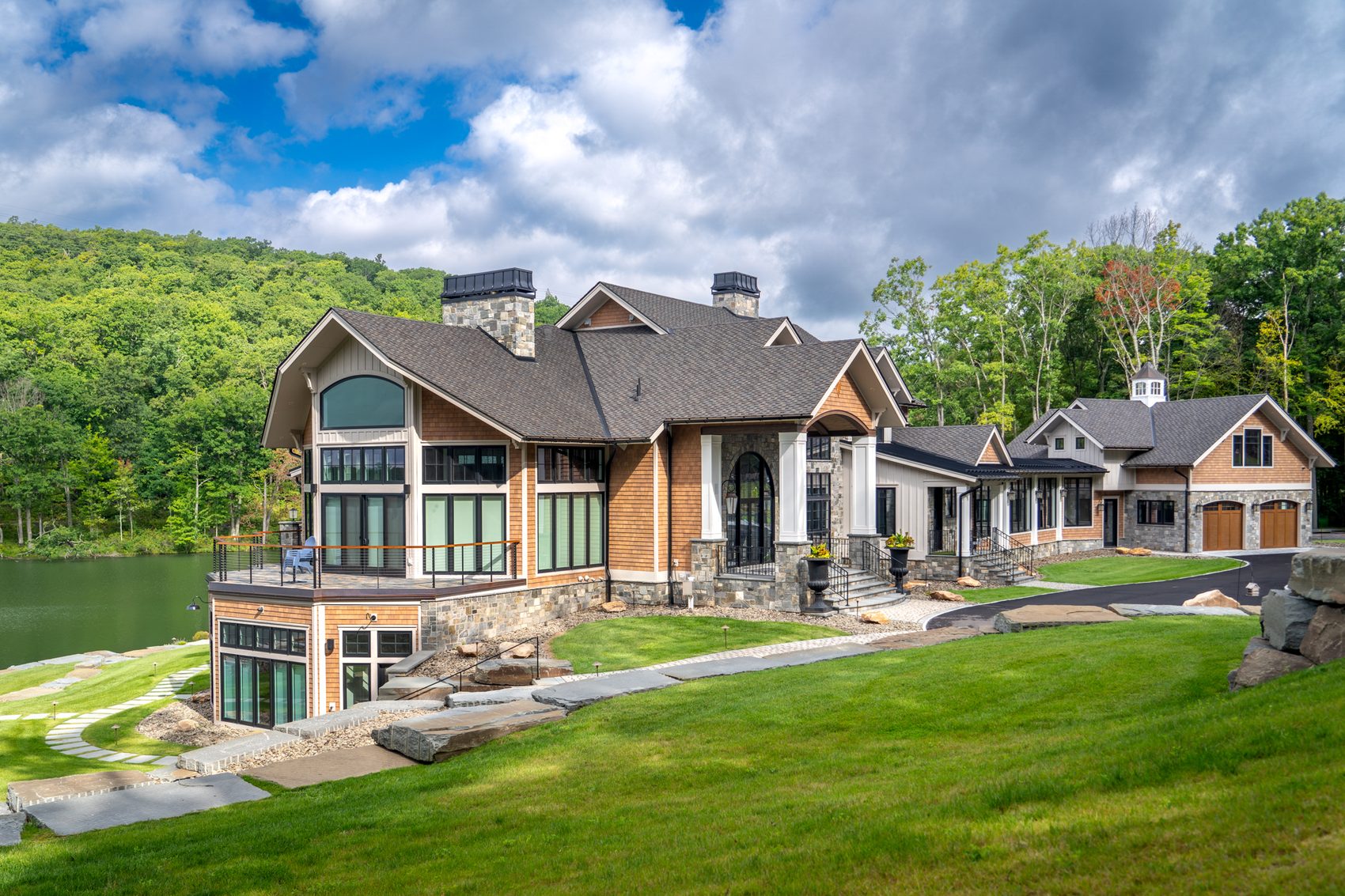 A lakeside custom home with a dark shingle roof over gables, dormers and a long glassed-in porch